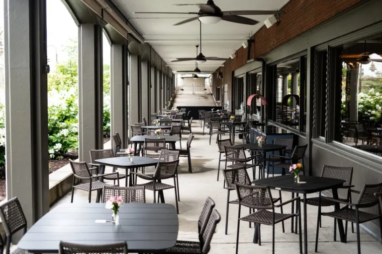 Outdoor patio at a restaurant with black tables and chairs, flower arrangements on tables, and blooming white hydrangeas in the foreground.